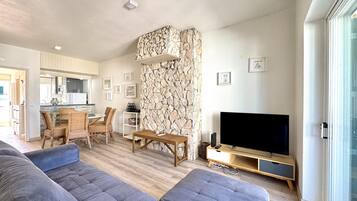 A modern living room with a stone accent wall, a flat-screen TV, and a dining area with wicker furniture.
