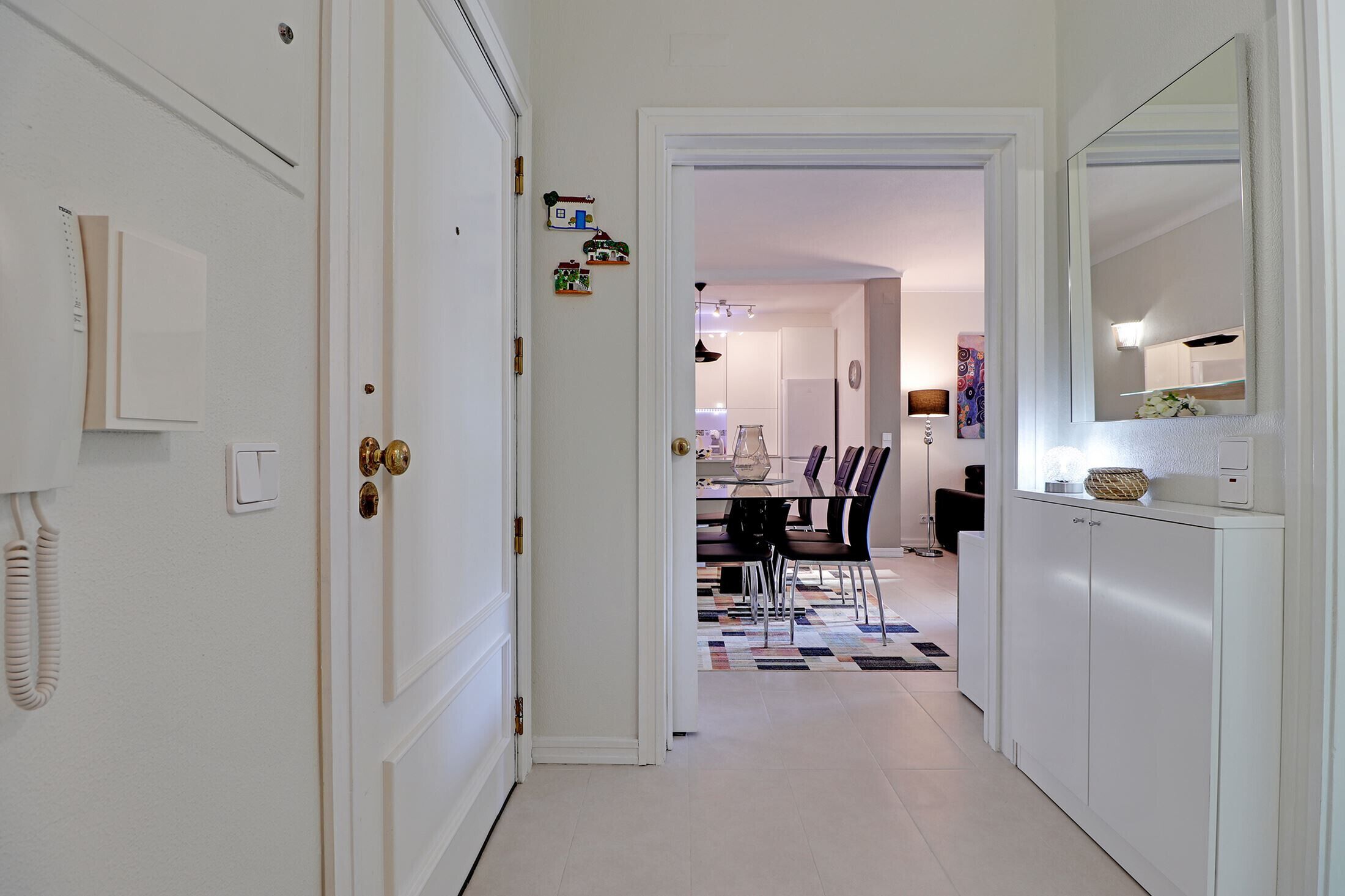 A hallway leading to a dining area with a checkered floor, white walls, and a door with a telephone.