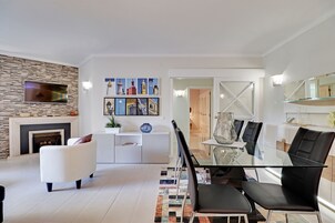 Uma sala de estar moderna com lareira, sofá branco, mesa de jantar de vidro e cadeiras pretas.