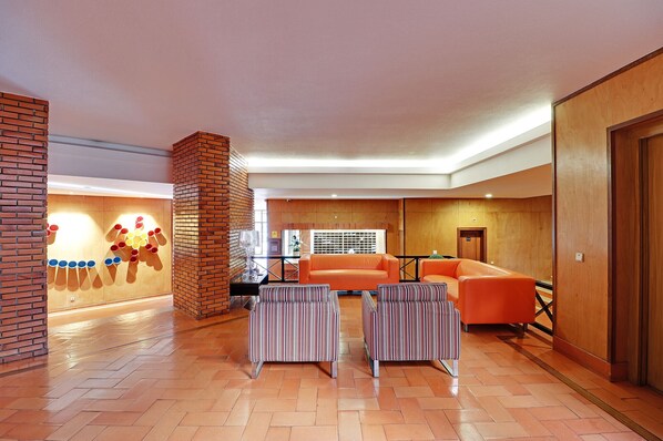 En modern entréhall med en tegelbeklädd accentvägg, ett receptionsbord i trä och en sittgrupp med randiga stolar och en orange soffa.