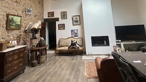 Amplia sala de estar con pared de piedra, un sofá, chimenea y comedor con mesa y sillas.