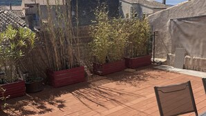 A wooden deck with red planters, a metal chair, and a view of buildings in the background. - Appartement Climatisé Avec Terrasse à Vidauban (Vidauban)