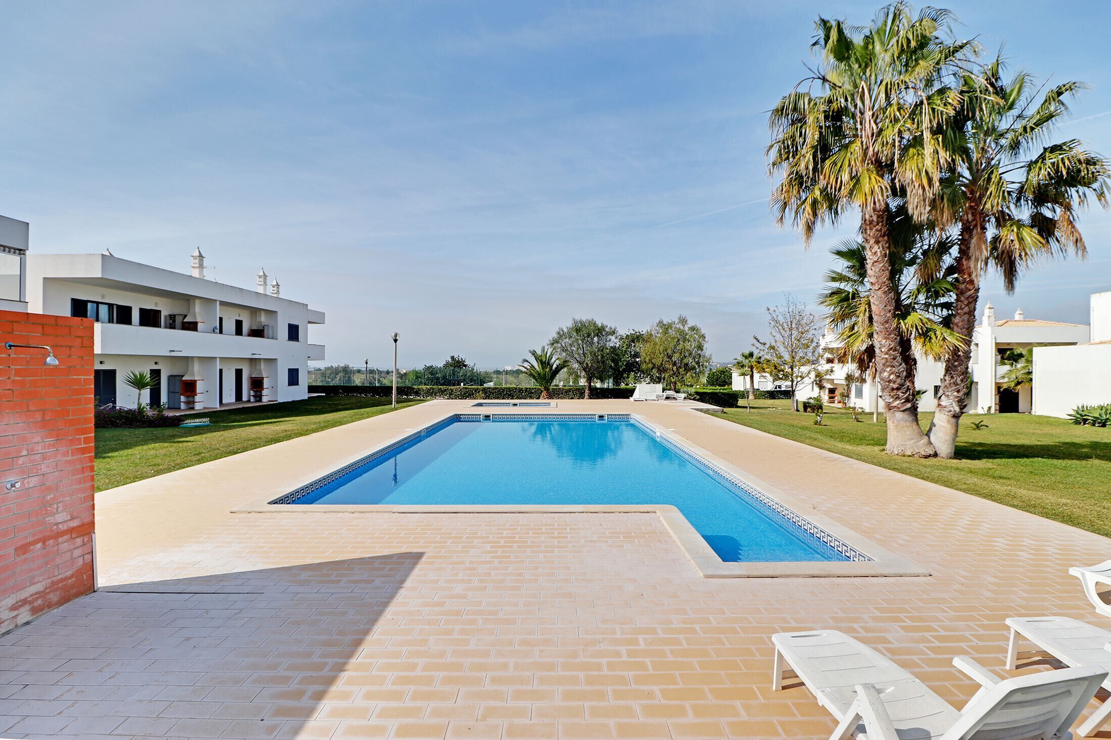 Una piscina rectangular amb vora de rajola, envoltada per un paviment de maó.