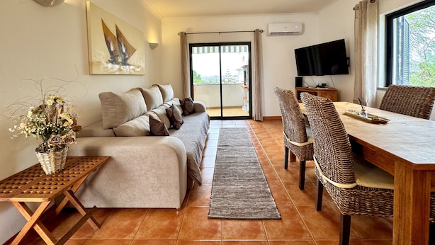 A living room with a sofa, a dining table with chairs, a TV, and a balcony door. - Pera Sea View With Pool by Homing (Silves)
