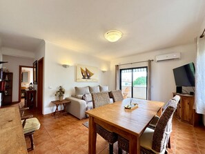 A living room with a sofa, a dining table with chairs, a TV, and a large window. - Pera Sea View With Pool by Homing (Silves)