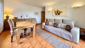 A living room with a wooden dining table, wicker chairs, a grey sofa with patterned cushions, a rug, and a painting on the wall. - Pera Sea View With Pool by Homing (Silves)