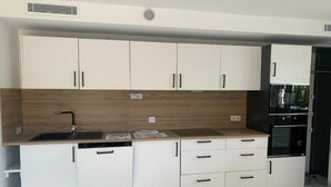 Eine moderne Küche mit weißen Schränken, einer Holzrückwand, einem schwarzen Spülbecken und einem eingebauten Backofen.