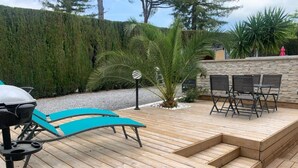 Eine Holzterrasse mit Grill, blauen Lounge-Stühlen und einer Steinmauer.