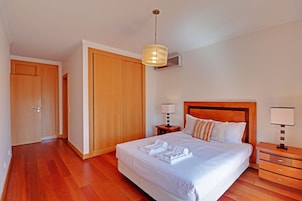 Un dormitorio ordenado con una cama grande, un armario de madera, mesitas de noche y una lámpara colgante.