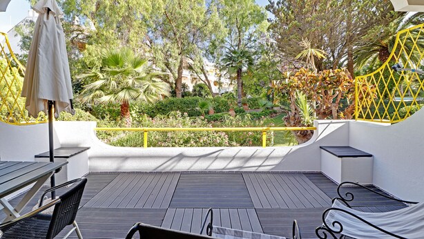 Eine Terrasse mit Blick auf einen Garten, mit einem Tisch, Stühlen, einem Sonnenschirm und einem gelben Gel änder.
