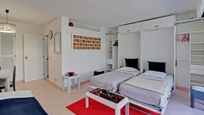 Ein modernes Hotelzimmer mit zwei Betten, einem Kleiderschrank, einem kleinen Tisch und einem roten Teppich.