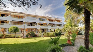 Ein mehrstöckiges Hotel mit Balkonen, einem gepflegten Garten und einem gepflasterten Weg.