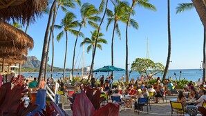 Un restaurante frente a la playa con terraza al aire libre, palmeras y vistas al océano.