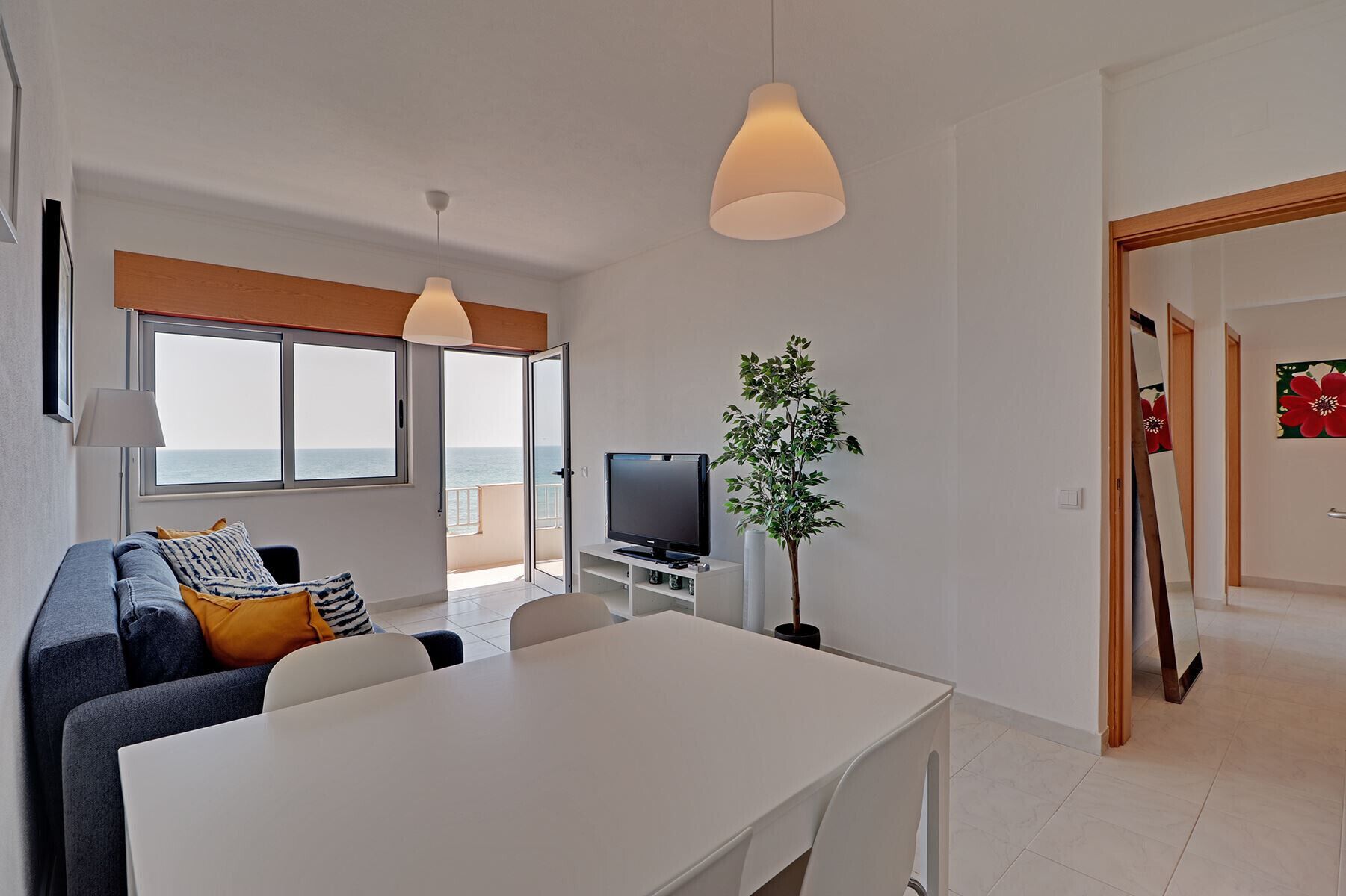 Ein modernes Wohnzimmer mit Sofa, Esstisch, Fernseher und Meerblick.