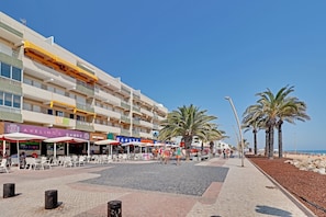 A beachfront hotel with outdoor seating, palm trees, and a clear sky. - Quarteira Beach & Ocean View 1 by Homing (Loulé)