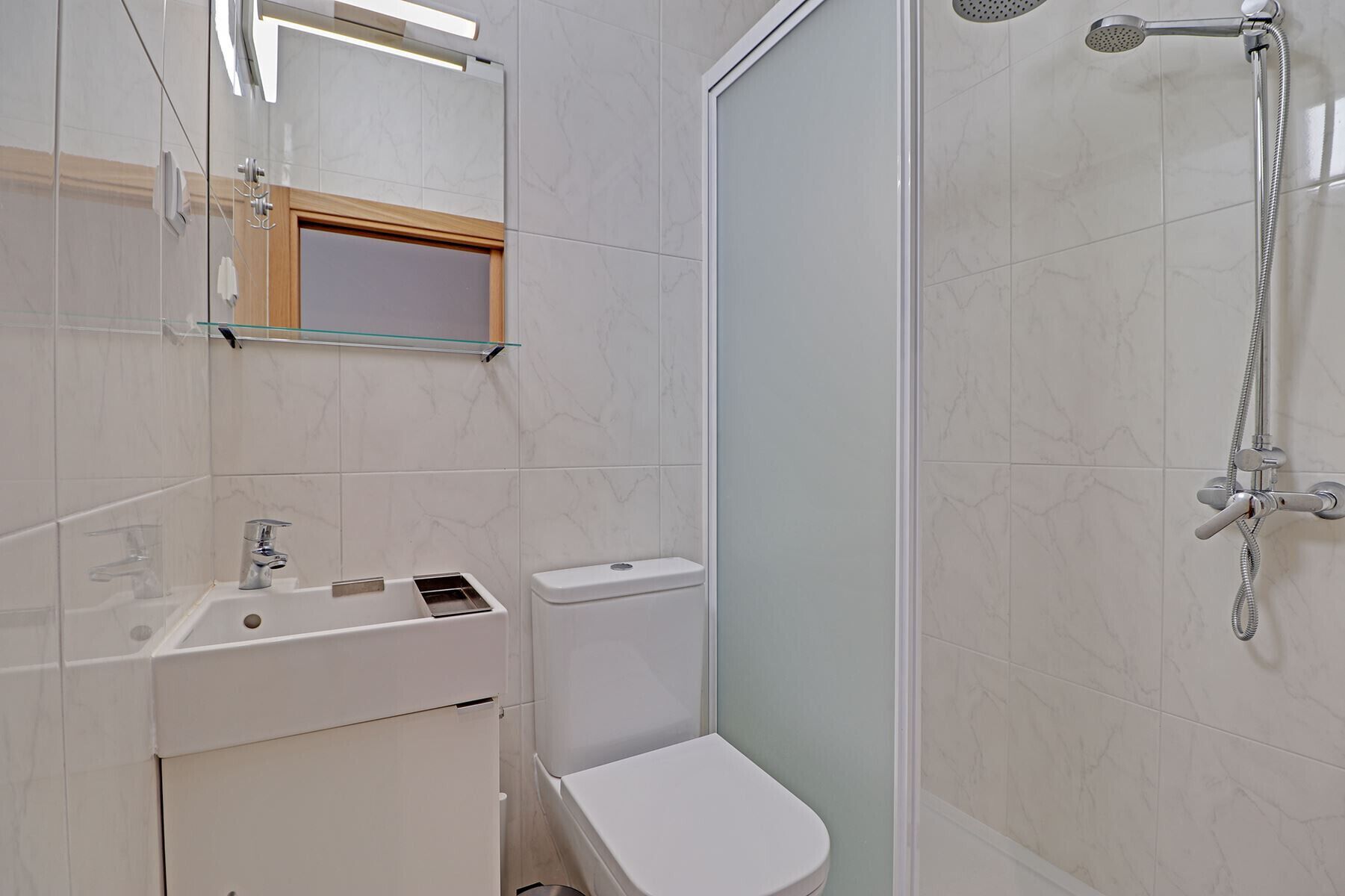 Un baño moderno con cabina de ducha de vidrio, un lavamanos blanco y un inodoro.