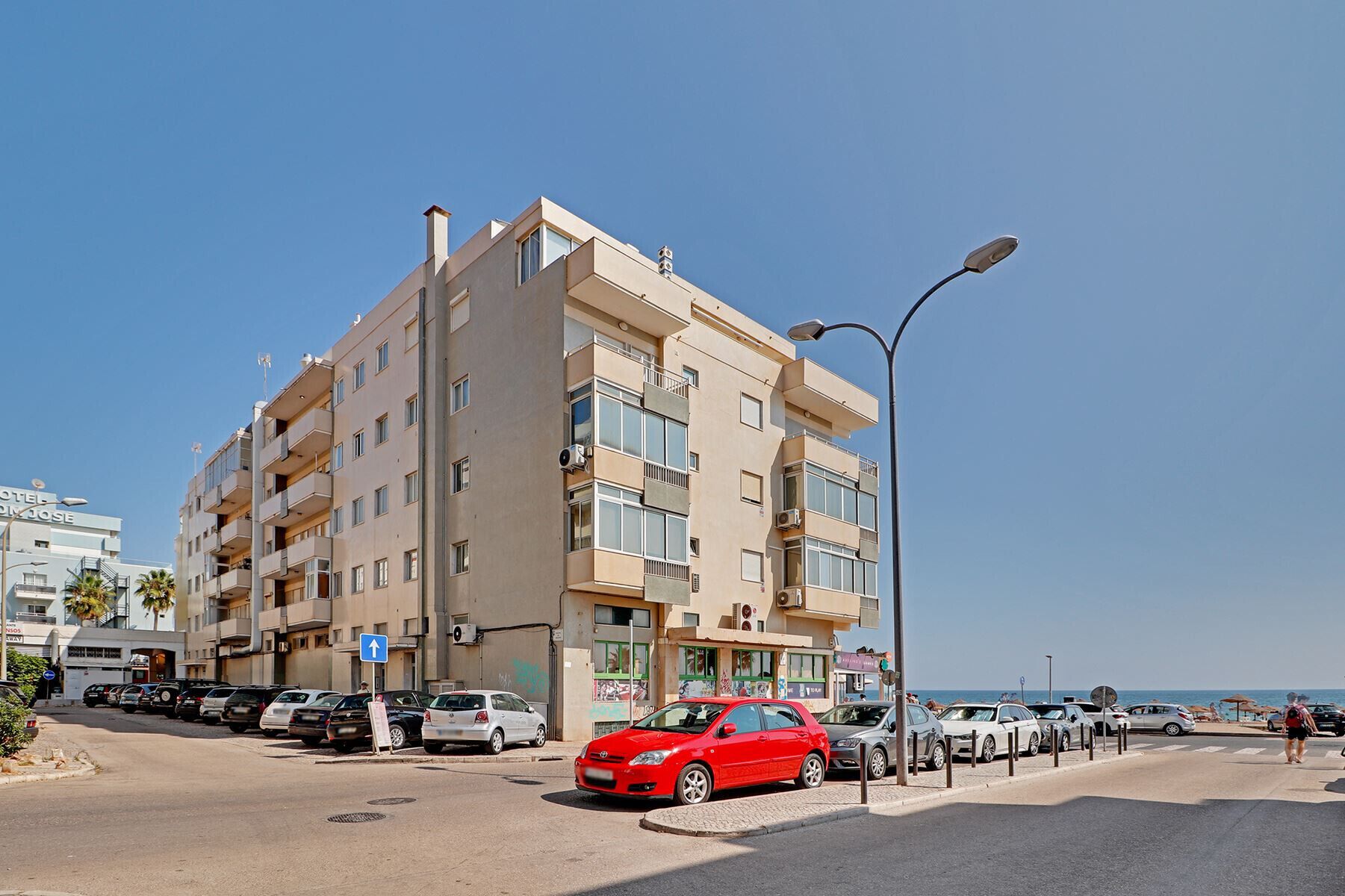 Hotel de varios pisos con balcones, estacionamiento y vista despejada a la playa.