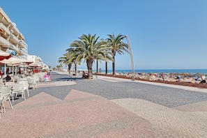 A beachside promenade with palm trees, outdoor seating, and a view of the sea. - Quarteira Beach & Ocean View 1 by Homing (Loulé)