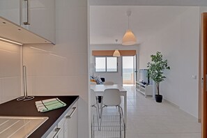 A modern kitchen with a dining area, a TV, and a potted plant. - Quarteira Beach & Ocean View 1 by Homing (Loulé)