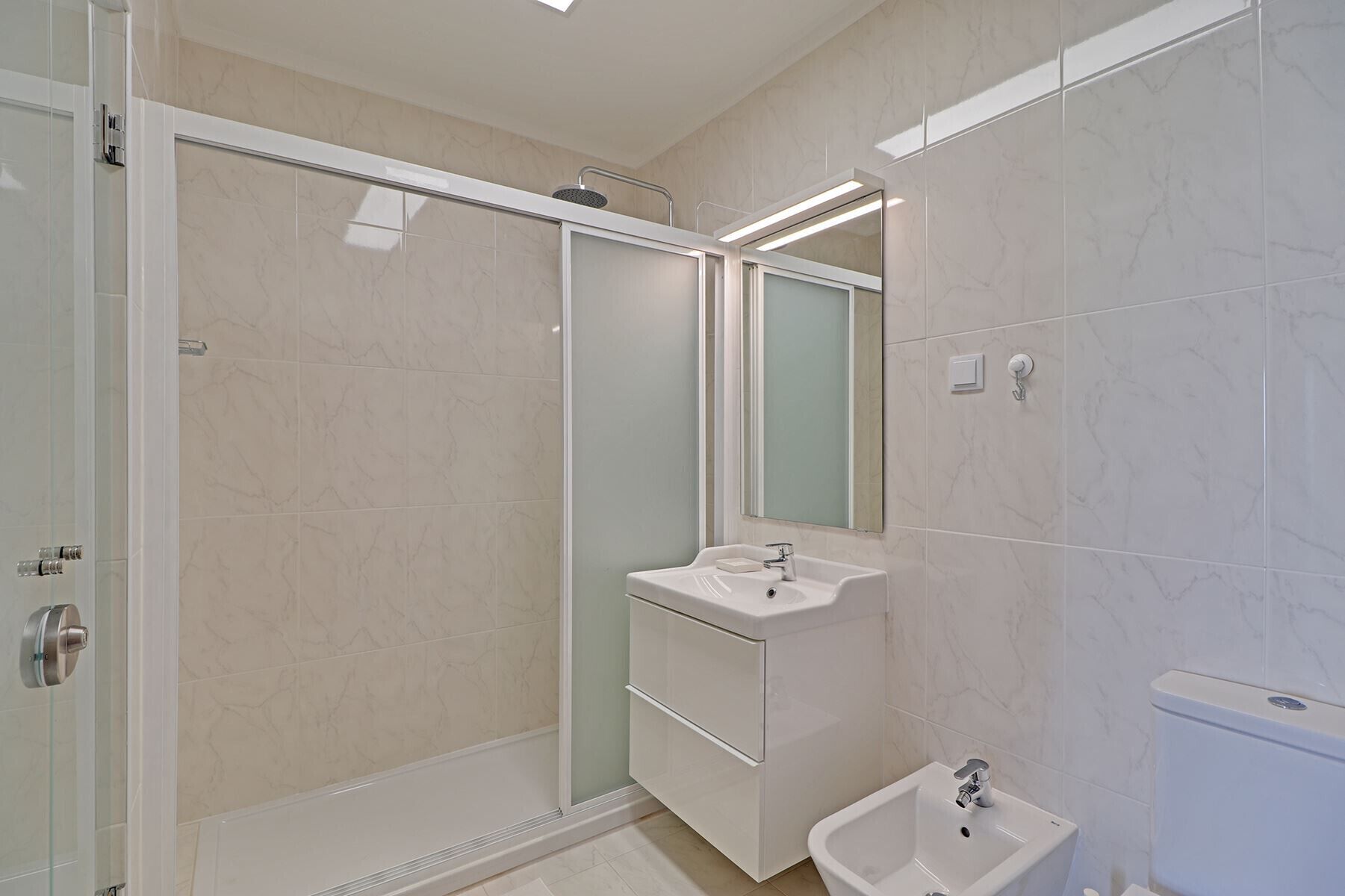 A modern bathroom with a glass-enclosed shower, a vanity with a mirror, and a separate sink.