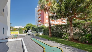 A courtyard with a croquet court, a palm tree, and a building with balconies. - Armação DE Pera Central by Homing (Silves)