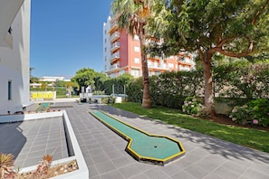 A courtyard with a croquet court, a palm tree, and a building with balconies. - Armação DE Pera Central by Homing (Silves)