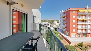 A balcony with a table and chairs, a view of a red building with balconies, and a clear blue sky. - Armação DE Pera Central by Homing (Silves)