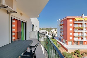 A balcony with a table and chairs, a view of a red building with balconies, and a clear blue sky. - Armação DE Pera Central by Homing (Silves)