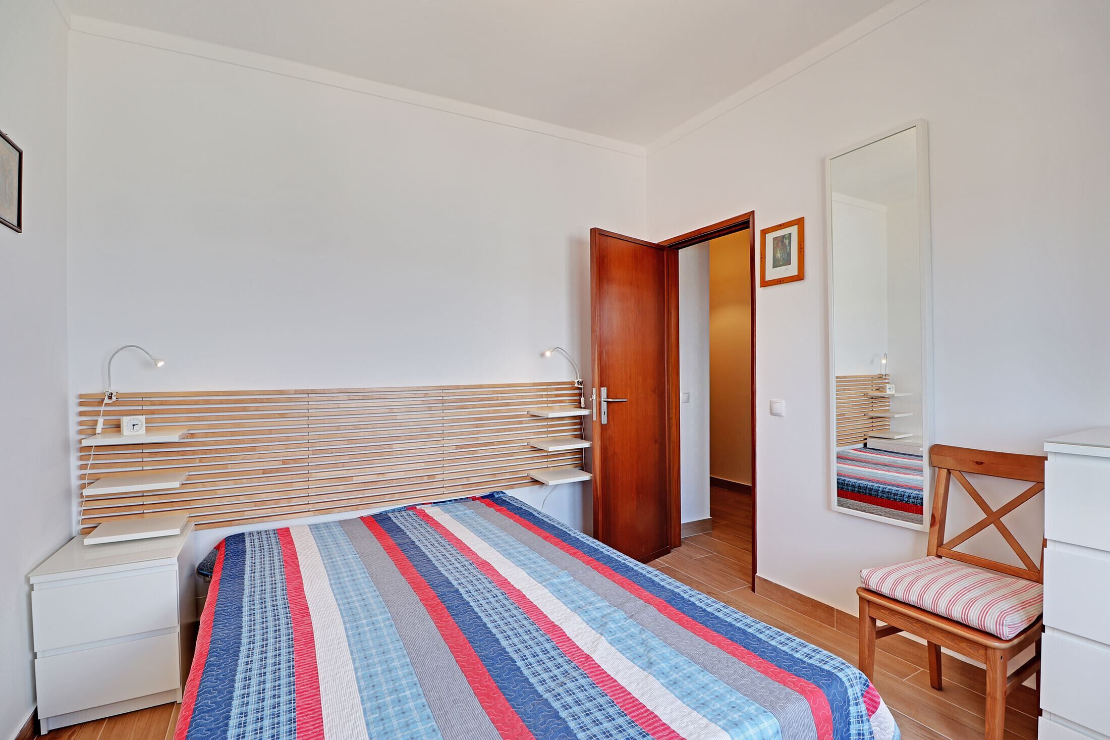 Une chambre à coucher avec un lit, une table de chevet, une chaise et un miroir.