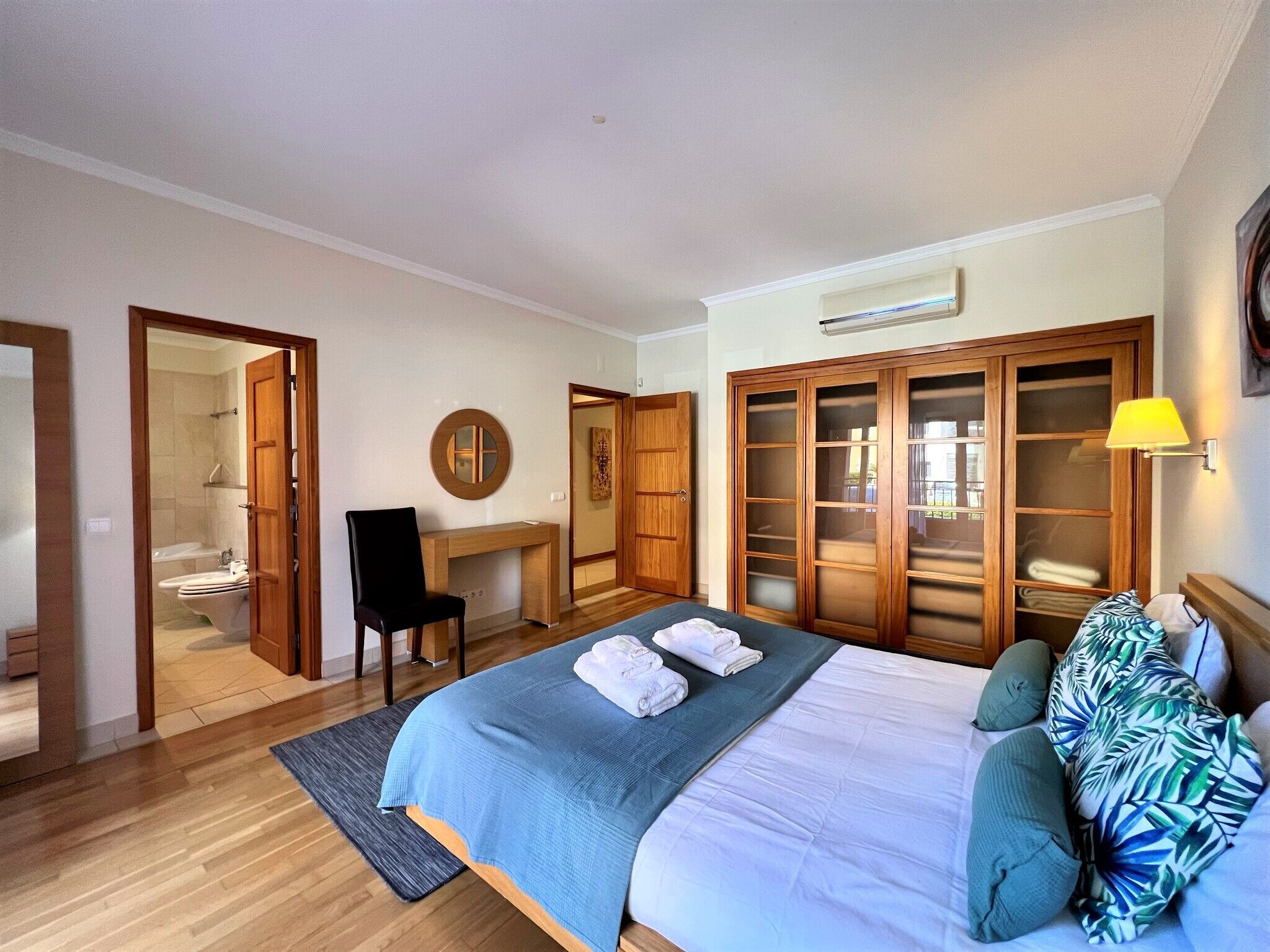 A bedroom with a bed, a desk, a chair, a wardrobe, and a bathroom visible through an open door.