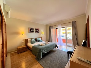 A hotel room with a bed, bedside lamps, a small table, a chair, and a view of the outside. - Vilamoura Victoria Gardens With Pool (Loulé)