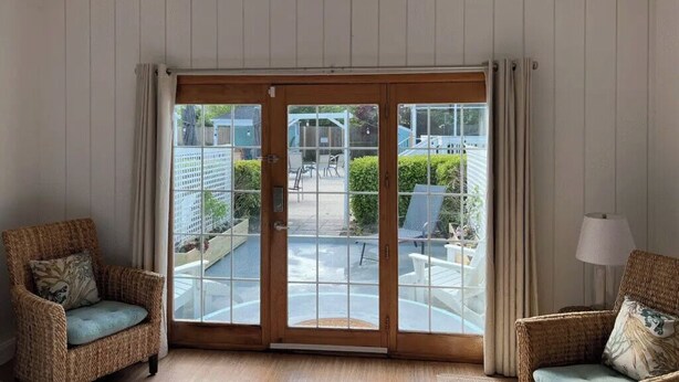 A room with a sliding glass door leading to an outdoor patio, wicker chairs, a lamp, and a window with a view of the outside.