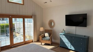 A room with a large sliding glass door, a wicker chair, a blue cabinet, and a mounted television.