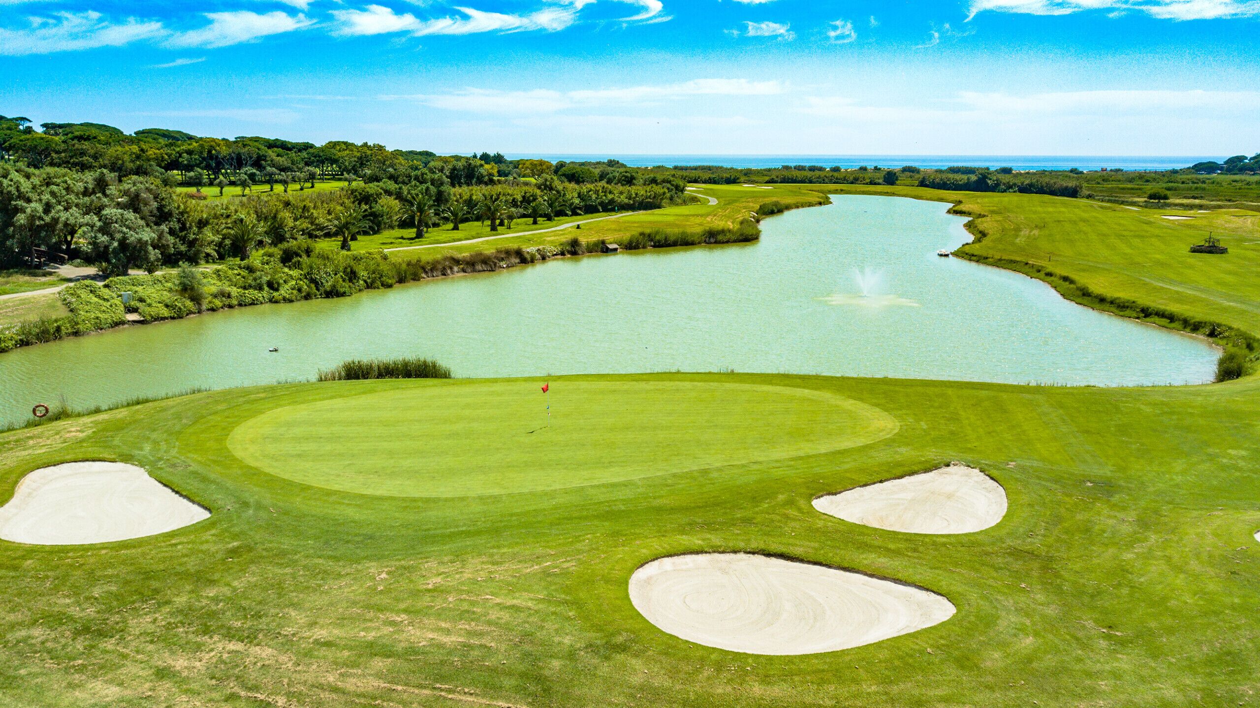 A golf course with a pond, sand bunkers, and a clear sky.