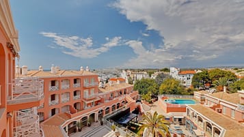 Un hotel con varios balcones, piscina y un patio con mobiliario exterior.