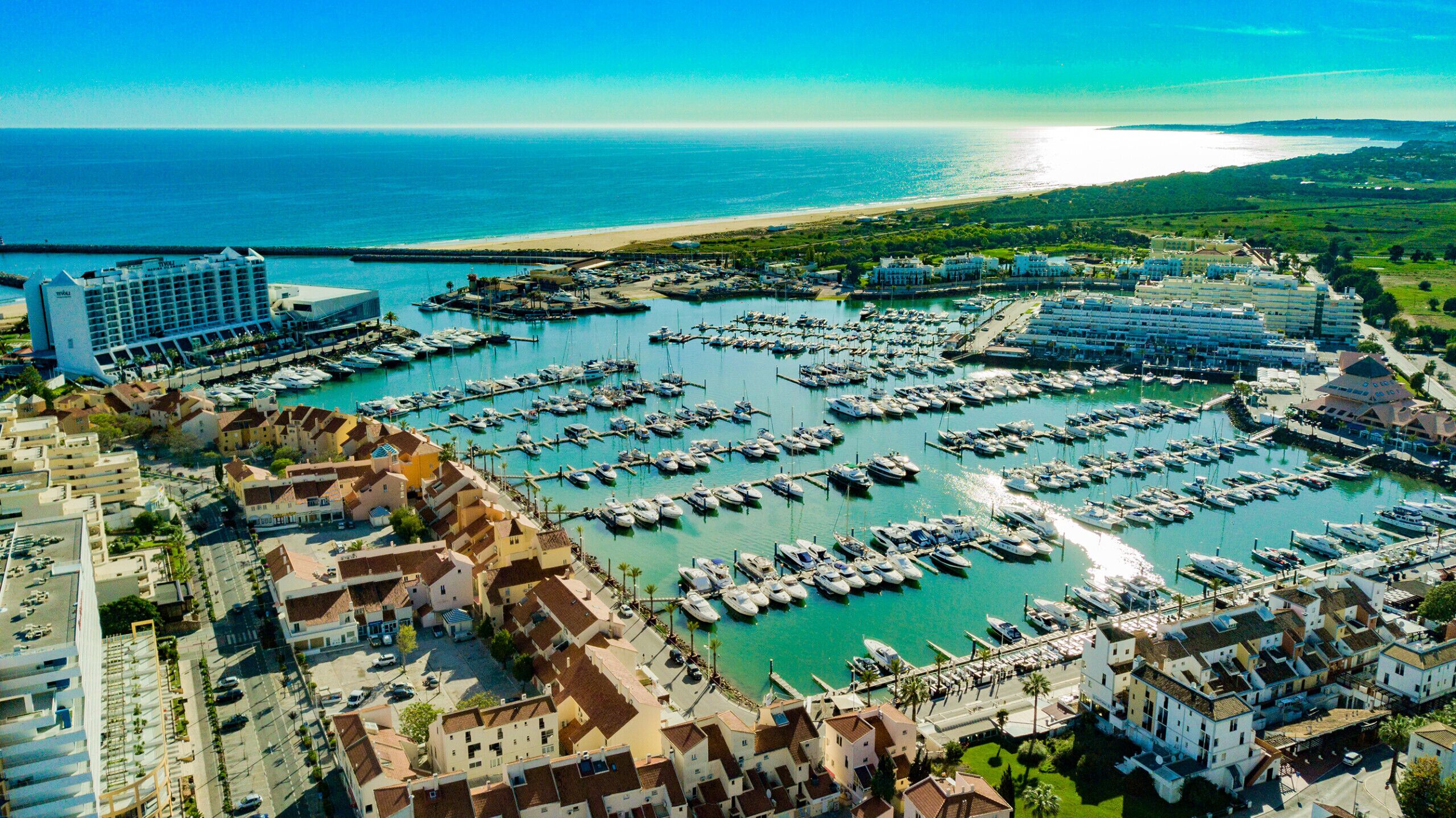 An aerial view of a marina with numerous boats docked, surrounded by residential buildings and a hotel.