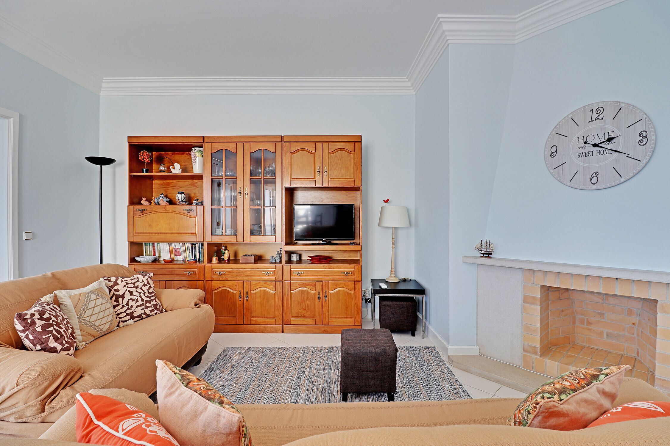 Una sala de estar con un sofá color beige, armarios de madera, un televisor y una chimenea.