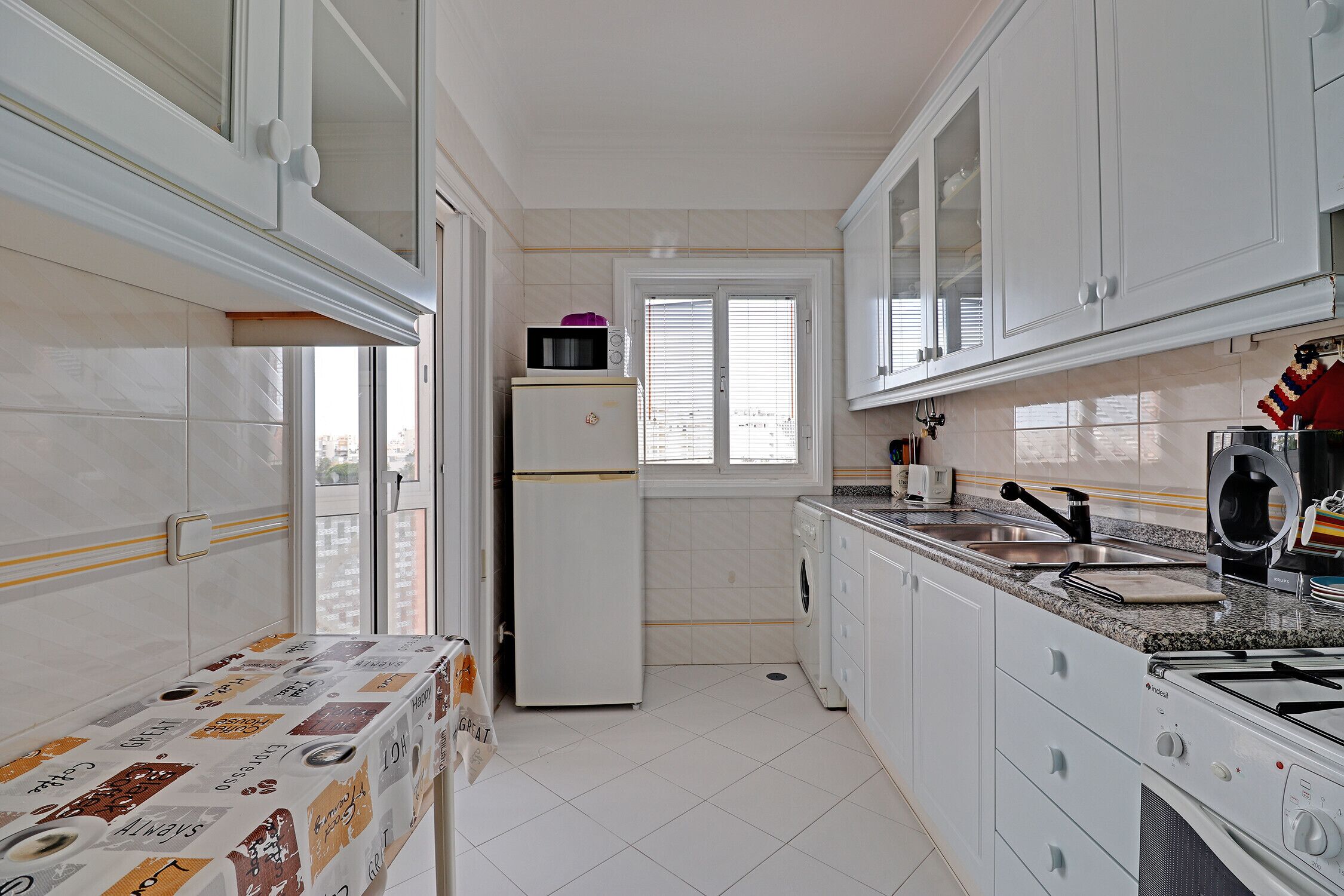 A compact kitchen with white cabinets, a refrigerator, a microwave, and a sink.