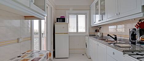 A compact kitchen with white cabinets, a refrigerator, a microwave, and a sink.