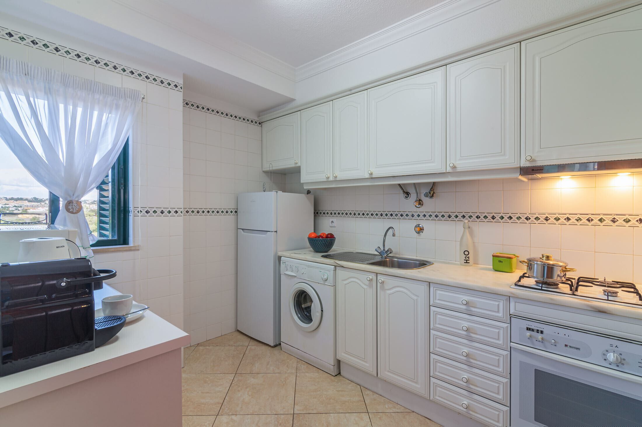 Cocina compacta con alacenas blancas, lavadora, lavaplatos y estufa.