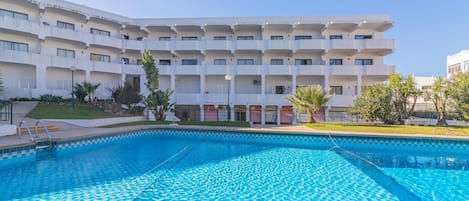 A swimming pool with a geometric tile pattern, surrounded by a building with multiple balconies and a flat roof.
