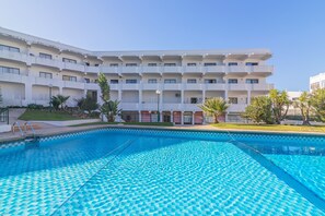 Ein Schwimmbecken mit geometrischem Fliesendesign, umgeben von einem Gebäude mit mehreren Balkonen und einer flachen Dachterrasse.