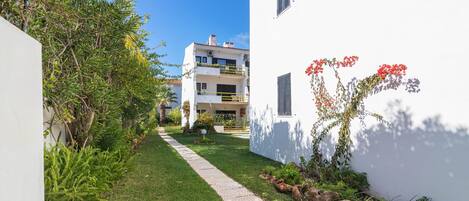 A pathway leading to a white building with a balcony and a garden with rocks and plants.