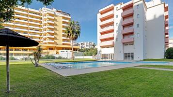 Un área de piscina con césped, una palmera y un edificio con varios balcones.