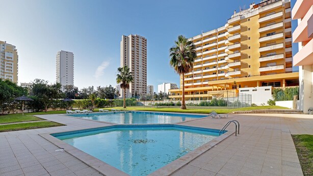 A swimming pool surrounded by a tiled patio area, with a tall building in the background. - Praia DA Rocha Central With Pool (Portimão)