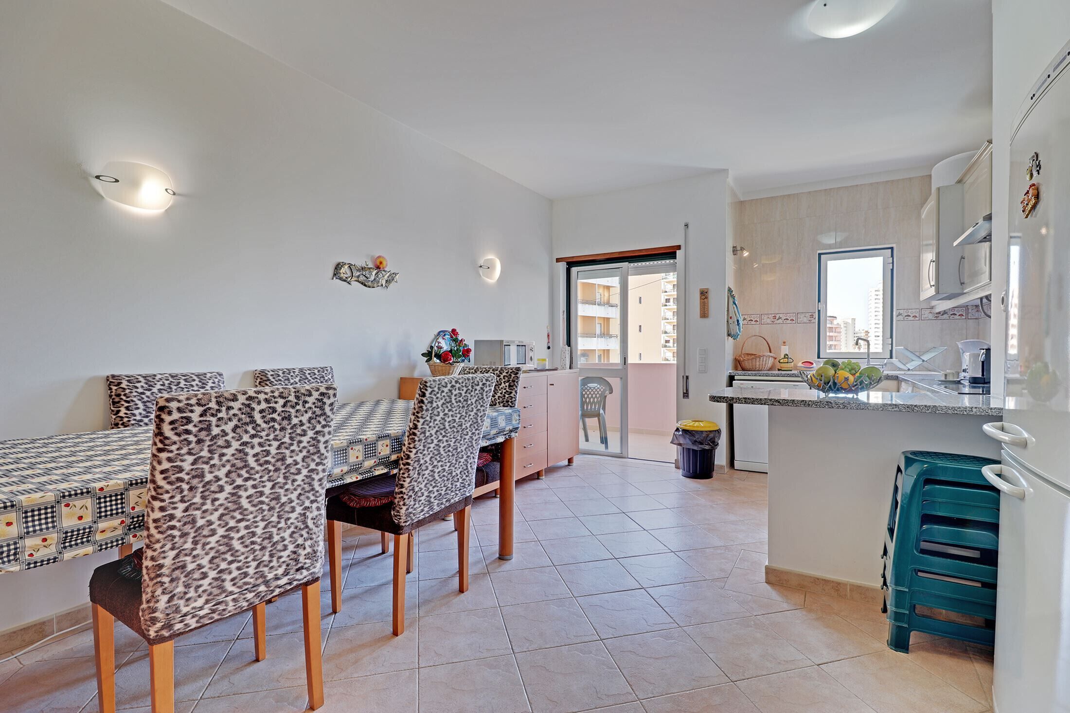 Un comedor con mesa y sillas, una cocina con pileta y armarios, y vistas de la ciudad a través de una puerta.