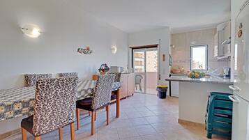 Un comedor con mesa y sillas, una cocina con pileta y armarios, y vistas de la ciudad a través de una puerta.