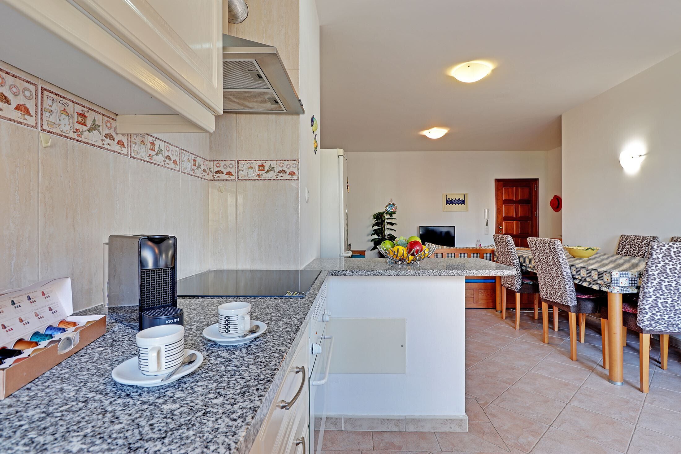 Eine moderne Küche mit Granit Arbeitsplatten, einem eingebauten Herd und einer Essecke mit gemusterten Stühlen und einer zentralen Kücheninsel.