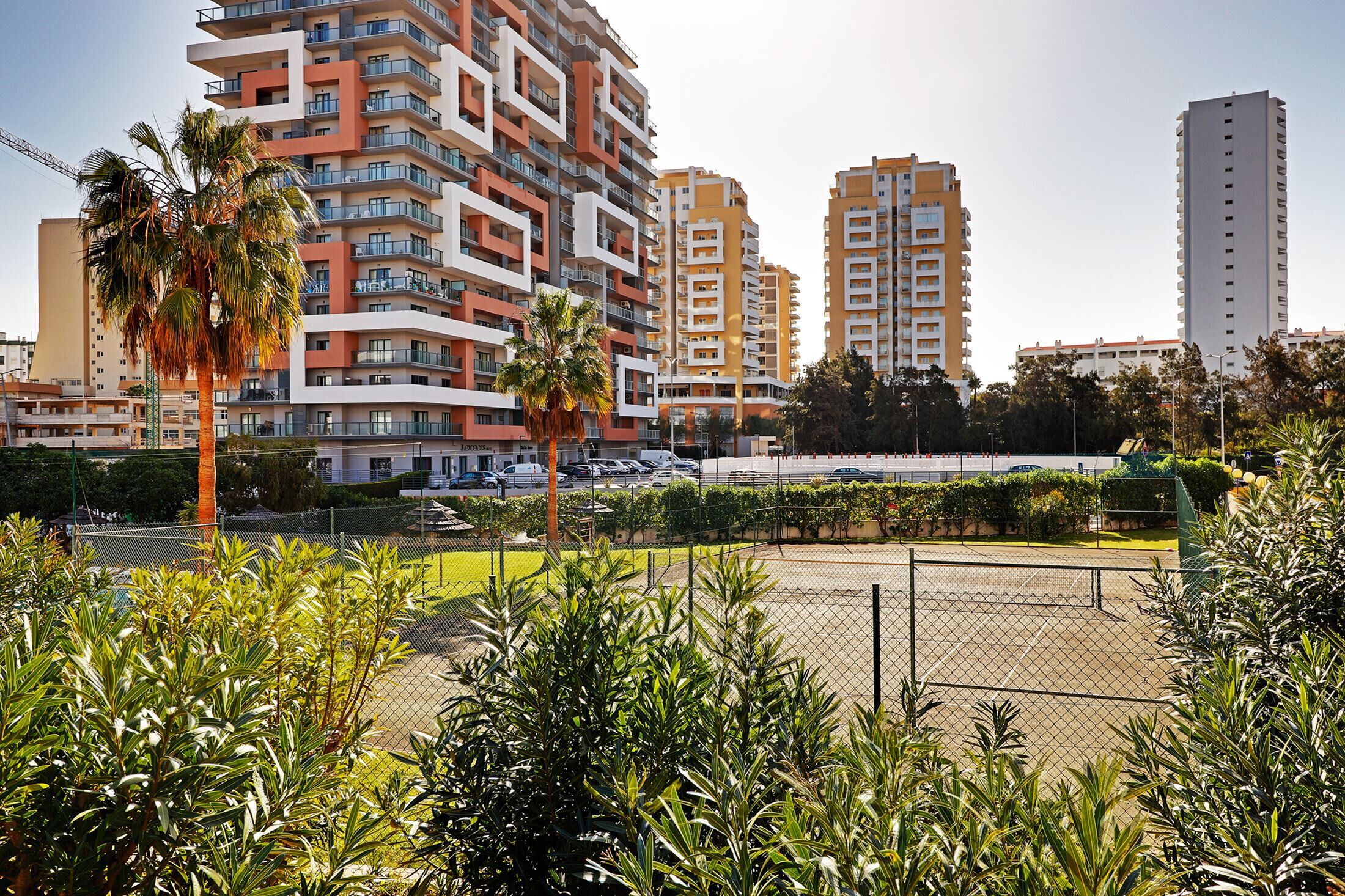 Área residencial com edifícios altos, quadra de tênis cercada e palmeiras.