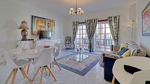 A modern living room with a dining area, a chandelier, and a large window with curtains. - Portimão Solar DO VAU With Pool (Portimão)